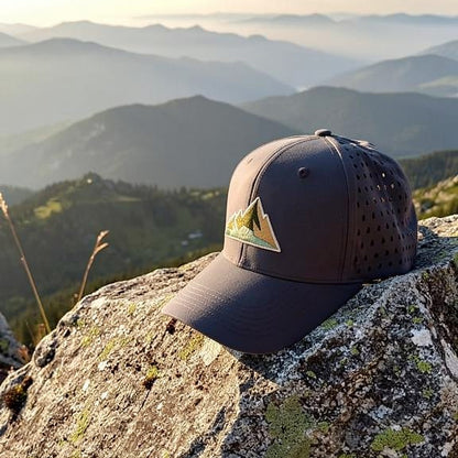 Graue bawearia Outdoor-Cap liegt auf einem Felsen vor einer weiten Berglandschaft im weichen Sonnenlicht.