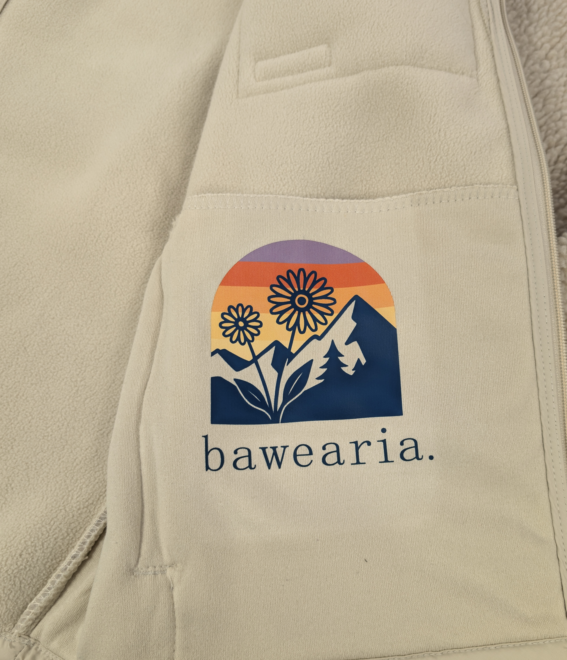 Detailaufnahme des bunten Innenprints einer beigen Teddy-Fleece-Jacke, der ein Retro-Bergmotiv mit Blumen und dem bawearia-Schriftzug zeigt