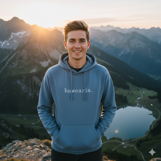 Herr steht lächelnd vor Bergpanorama mit See und trägt einen beigen bawearia Hoodie mit Logo-Schriftzug auf der Brust